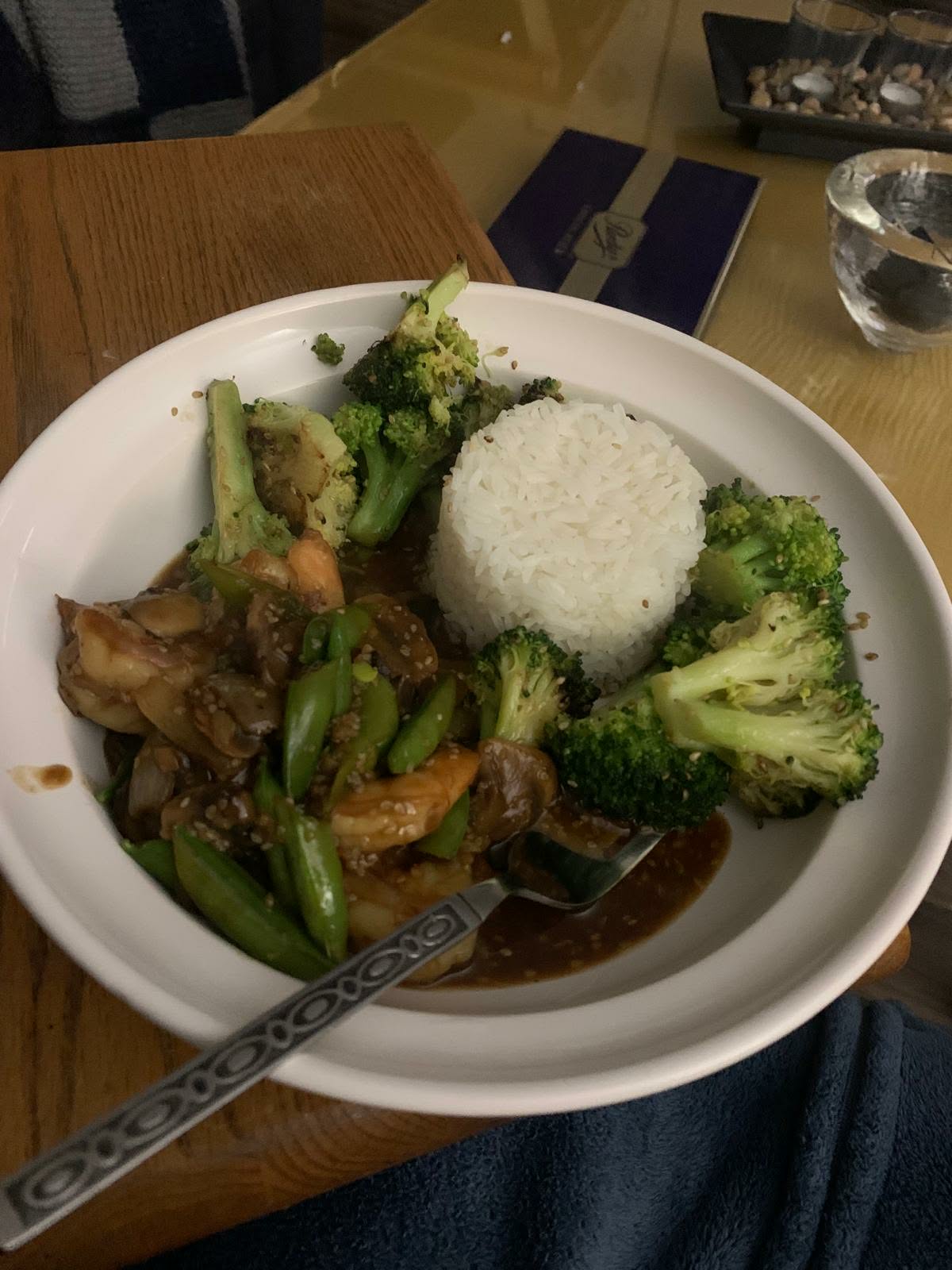 Shrimp stir-fry with snap peas and mushrooms in a dark sauce, served with broccoli and molded white rice in a white bowl
