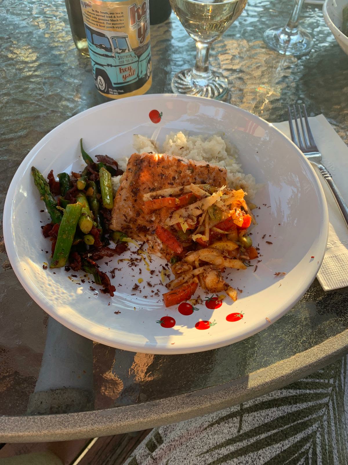 Seared salmon topped with shredded vegetable slaw, served with rice and asparagus in a white bowl on a sunny patio table