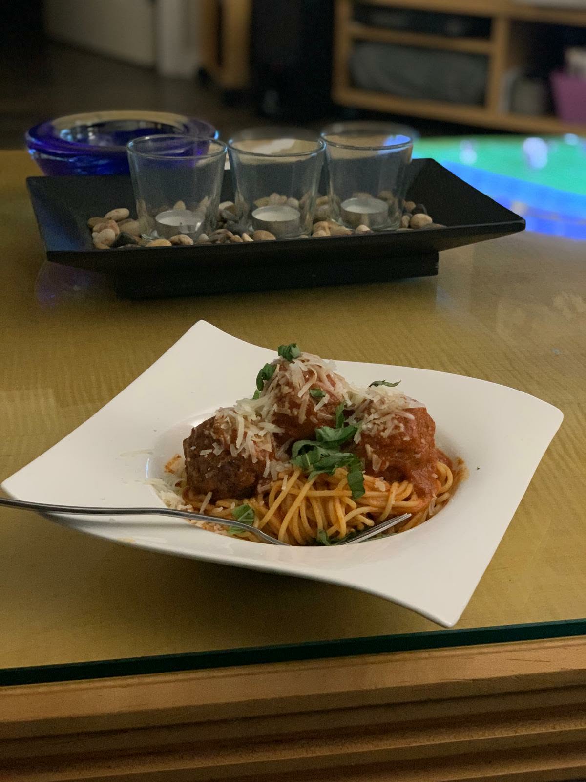 Spaghetti with meatballs, grated parmesan and torn basil in a white square bowl